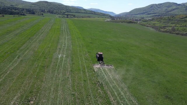 Agricultural tractor preparing land with a harrow for the new season. Beautiful green landscape with mountains in the background