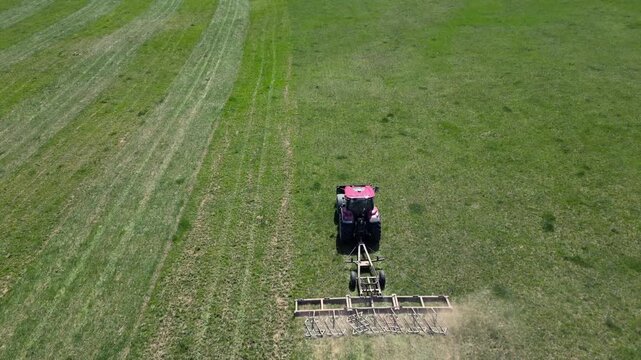 High angle view of a modern tractor with a harrow attachment cultivating agricultural land, preparing the soil for planting crops