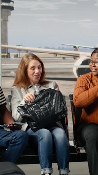 Vertical video Going to boarding gate, departure board timetable and tourists in airport hub. Reading time on FIDS display, boarding call and multiethnic travelers on lounge benches leaving