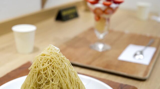 絞りたて生モンブランのクローズアップ 背景にいちごパフェのあるカフェの風景