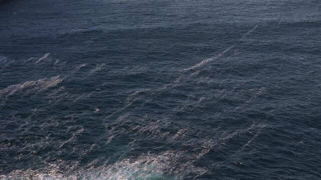Observe the expansive dark blue ocean water stretching out under clear daytime light. Gentle waves and ripples cover the surface as a small red buoy floats calmly amidst the open sea.