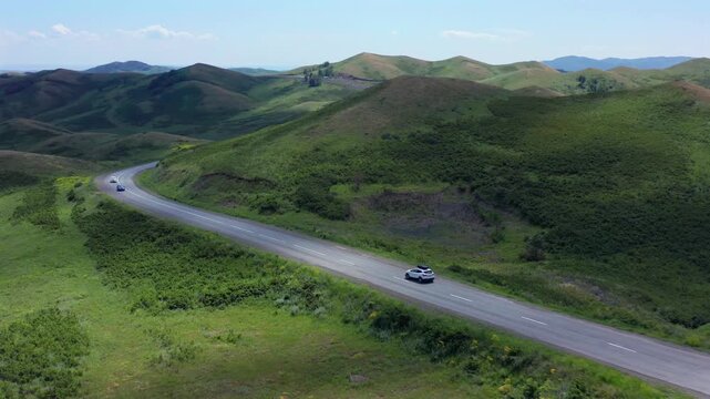 Epic aerial drone shot of car driving along winding road through green hills in Kazakhstan, powerful road trip concept symbolizing freedom, escape, adventure, independence, limitless travel lifestyle.