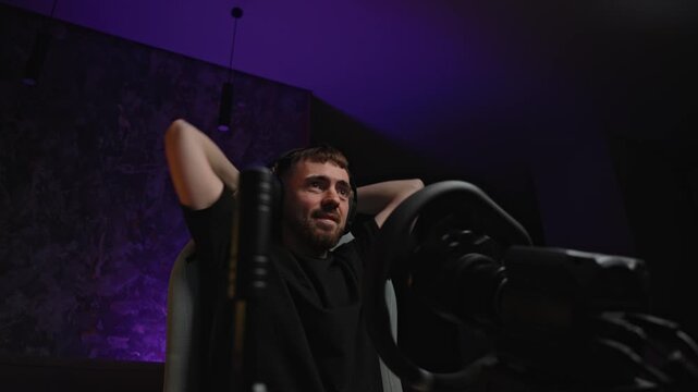 White streamer stretching in purple studio, headset on, microphone visible, reclining in gaming chair after live broadcast