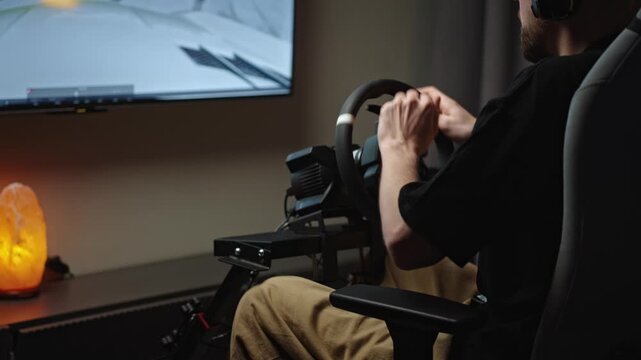 Man steering wheel in racing simulator, calm evening home setup with headset and monitor, learner driver practicing turns