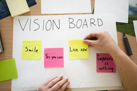 Hands, woman and writing on vision board in home for planning goals, aspirations and manifestation. Poster, pictures and sticky notes for inspiration, progress tracking and personal development
