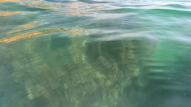 Seawater ripple seabed reveals a clear view of the rocky ocean floor beneath transparent turquoise waves on a calm day