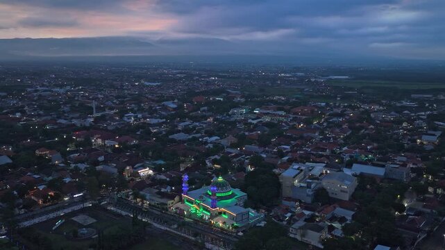 Green illuminated mosque in probolinggo cityscape at sunset