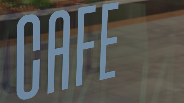 Closeup of cafe decal on glass, soft reflections of street and interior, warm sunlight, shallow depth of field, modern typography, subtle bokeh, cinematic k slow motion mood