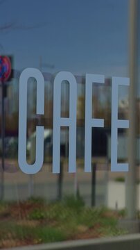 Cafe sign closeup. Upscaled view of storefront lettering. Detailed shot of cafe branding on glass. Highresolution slow motion image showcasing modern cafe name with soft outdoor backdrop
