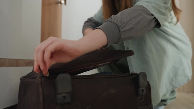 Preparing for journey quietly. Woman organizing travel items meticulously. Caucasian woman methodically packing her weathered suitcase with clothing and essentials in calm entry setting