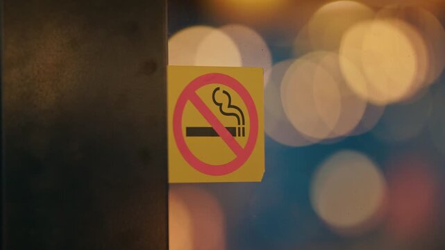 No smoking sticker on glass, cinematic k slow motion footage captures warm blurred lights of city interior behind reflective panel, shallow depth of field, soft color palette, ambient glow
