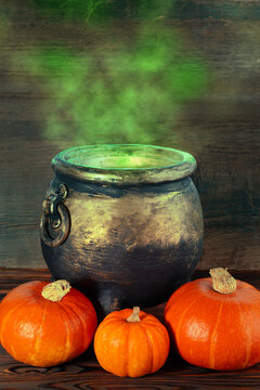 Halloween scene with old metal cauldron emitting glowing smoke and pumpkin on rustic wooden background. Dark composition with large copy space for design or advertising.