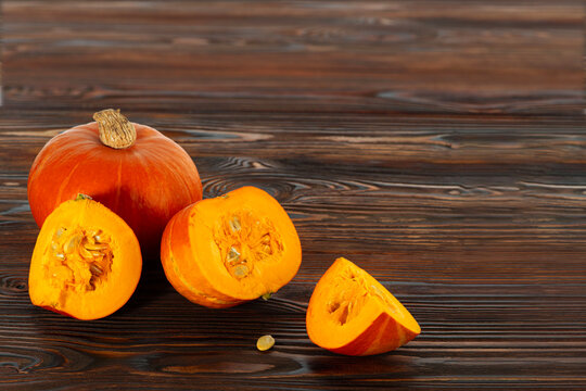 Fresh pumpkin Red kuri squash with cut slices and seeds on rustic wooden table. Raw autumn vegetable, natural ingredient for cooking, healthy food concept and seasonal harvest