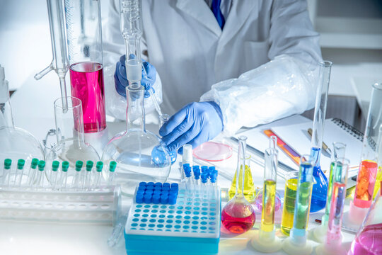 Gloved hand holding test tube in modern laboratory with sample vials and glassware under blue light, concept of research, biotech and clinical testing.