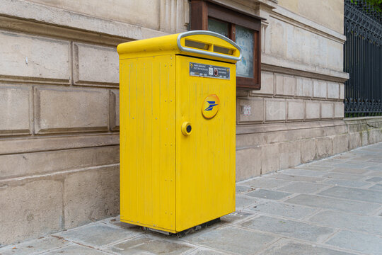 La Poste yellow mailbox stands beside a stone wall on a quiet Paris sidewalk