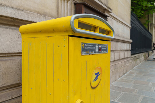 La Poste yellow mailbox stands beside a stone wall on a quiet Paris sidewalk