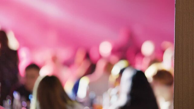 Pink stage lights illuminate dancing crowd at indie band performance, guitars and drums silhouetted with vibrant bokeh and slow motion crowd movement for cinematic concert footage