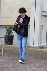 Teenage male walking across campus plaza checking watch holding pink folder and bag wearing hoodie © wavebreak3
