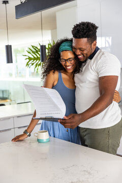 African American couple leaning at marble kitchen island, reading clipboard and holding teal mug