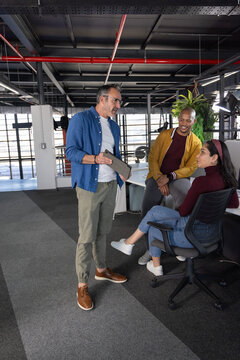 Diverse coworkers discussing project while standing and sitting in open-plan office with tablet