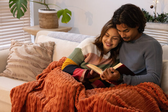 Diverse couple reading open book on light sofa sharing rust throw woman in striped sweater