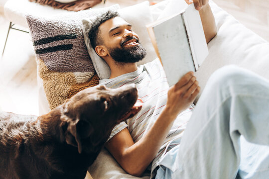 Man relaxing at home reading book with dog