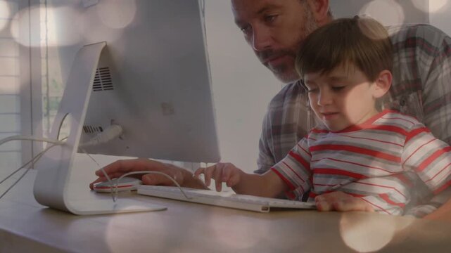 Boy tapping white keyboard, father guiding hand and moving wired mouse, sharing education moment