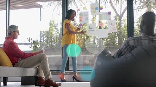 Leader pointing at charts moving sticky notes on glass wall causing business graphics sharing plan