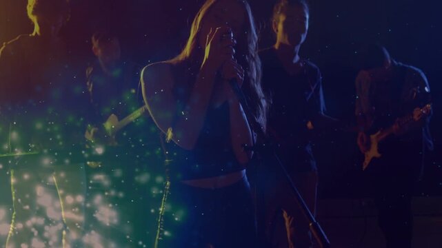 Camera pulling singer stepping to mic, singing in music rehearsal, guitars, particles drifting left