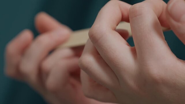 Expert practitioner performing detailed nail shaping process. Close view of professional meticulously shaping nails using beige file against teal background demonstrating expert hand care techniques