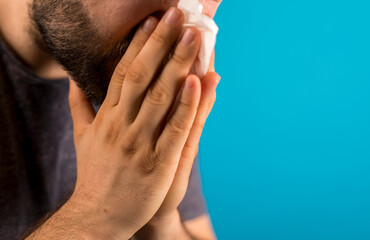 Fototapeta premium Close-up of a man using a tissue, capturing cold, sickness, or allergy symptoms against blue.