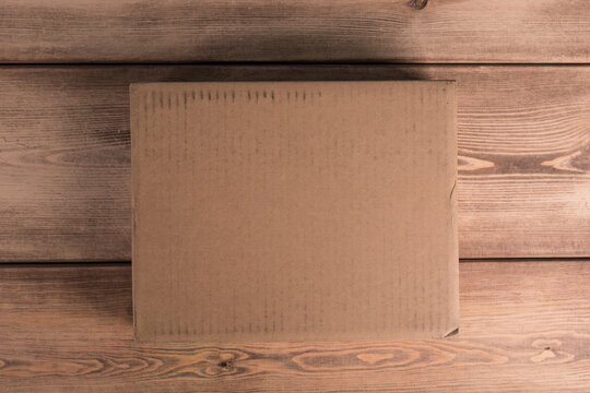 A plain cardboard box rests on a textured wooden surface, viewed from above