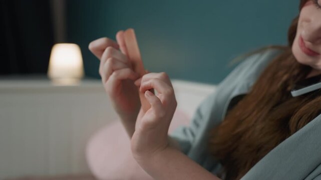 Closeup hands filing nails with emery board in soft bedroom light, intimate grooming action framed against teal wall and lamp concentrated motion, tactile texture and precision grooming evoke