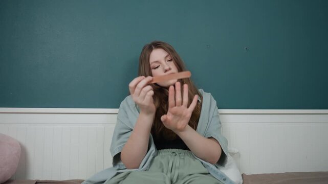 White woman concentrating on nails, teal wall and bed setting, focused expression, precise filing with emery tool, trainee practice vibe, casual clothing, soft cushion nearby, closeup hand movements,