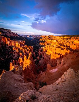 Dramatic golden sunset lighting over rugged canyon rock formations, orange sandstone hoodoos under blue twilight sky, nature landscape photography