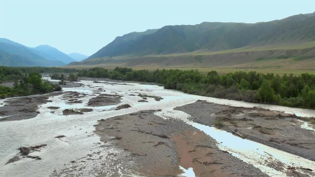 Braided river channels flow through gravel banks as drone flies forward over Chilik River valley, revealing wide mountain landscape with streams, greenery and natural terrain in Kazakhstan