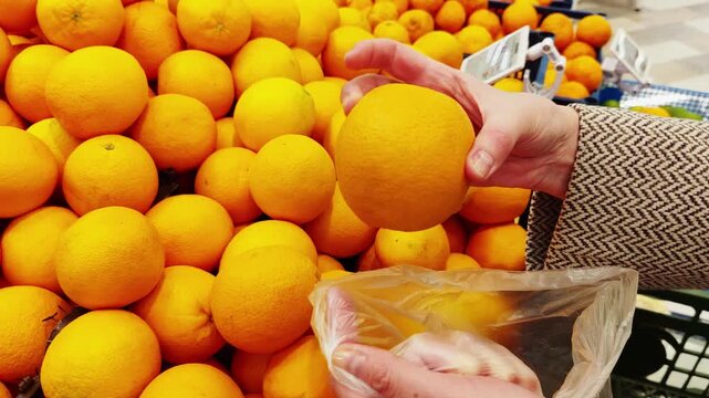 Woman Selecting Fresh Oranges At Supermarket Produce Section. Daily grocery shopping routine and fresh produce selection at a local store or market.