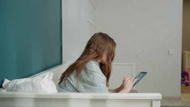 Student using device. Woman concentrated on digital learning. Young lady engaged with tablet in simple room. Female student focused on screen while studying in minimalist environment