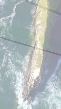 Vertical video: Camera tilting, waves foaming around long spit, grid shadow shifting, showing flow