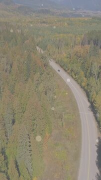 Vertical video: Dark vehicle pulling from roadside onto curved road, moving toward distant ridges