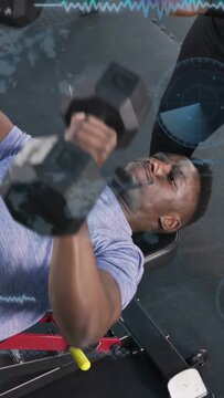 Vertical video: Man pressing dumbbells on bench on cue, spotter guiding for fitness, HUD hovering