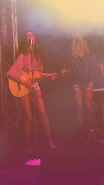 Vertical video: Singer starting song playing guitar singing at mic dancer moving by kit lights haze