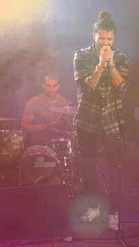 Vertical video: Drummer starting beat, singer gripping mic, singing under music haze to move crowd