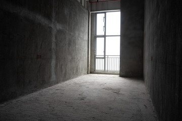 Naklejka premium Bare concrete corridor in an unfinished apartment with large window allowing natural light to enter