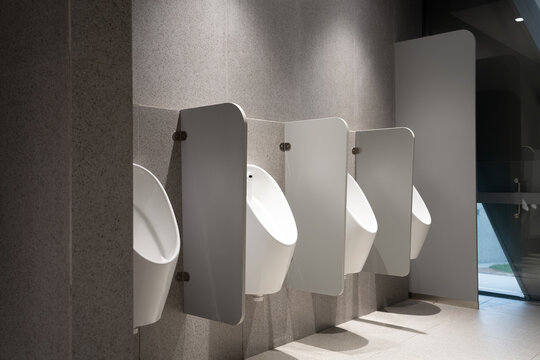 Modern public restroom with white urinals and privacy partitions mounted on gray textured walls