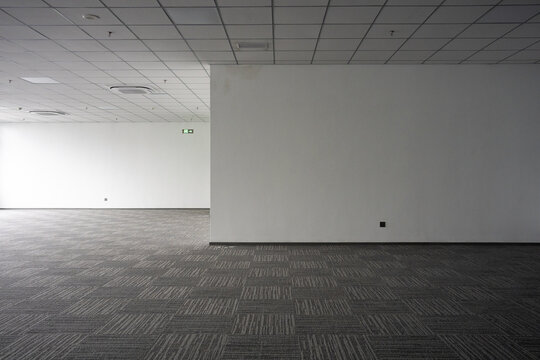 Empty office space with gray carpet flooring and white walls under grid ceiling