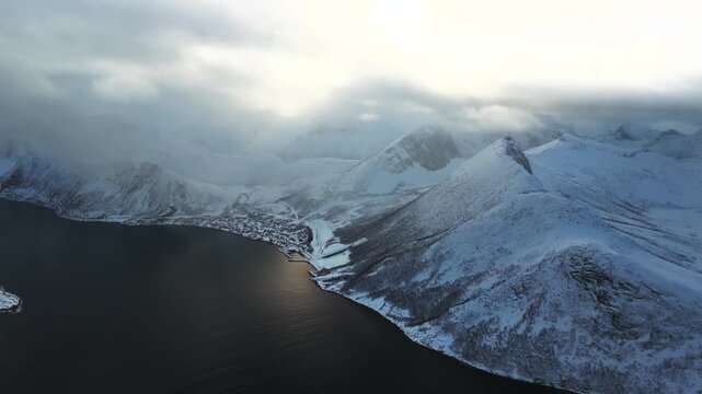 Drone shot of a snowy coastal village tucked between arctic mountains and sea