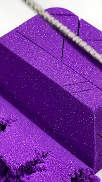 Extreme macro, a thin metallic wire slicing incredibly smoothly through a vibrant purple block of kinetic sand, completely satisfying and mesmerizing geometric texture crumbling perfectly, 4k.