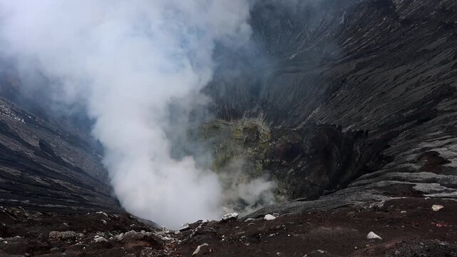 A powerful view looking down into an active volcanic crater, where thick white steam billows upward from deep within the vent. Mount Bromo in East Java, Indonesia