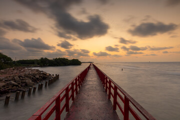 Obraz premium Long Red Wooden Bridge Stretching into the Ocean during Golden Sunset with Flying Seagulls,A perspective view of a vibrant red wooden pier leading towards the horizon over the sea.